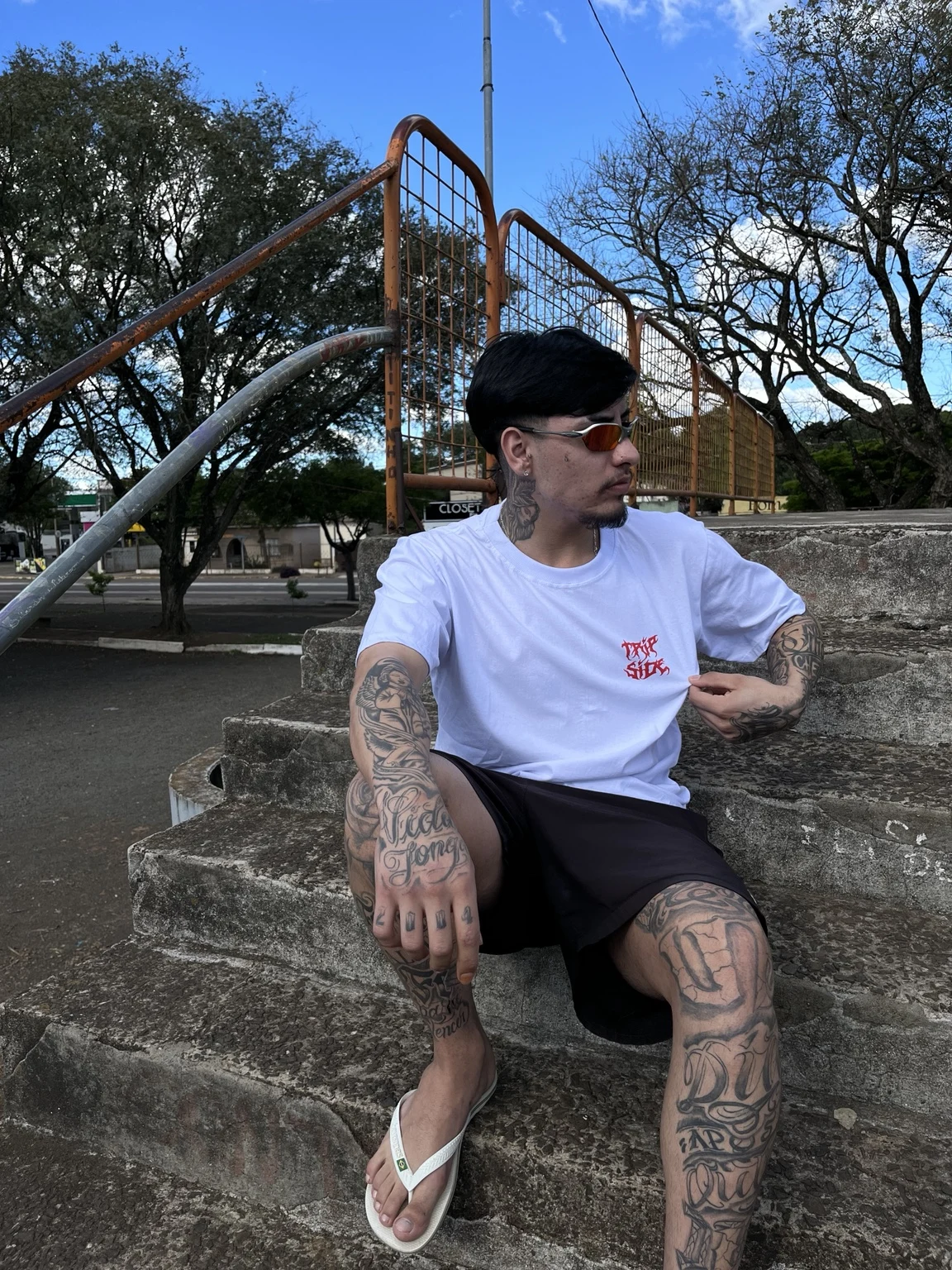Look WND com camiseta branca de estampa vermelha e bermuda preta, nas escadarias ao ar livre